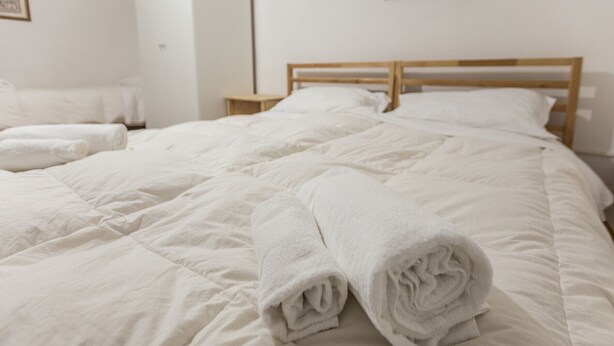 Un letto rifatto con lenzuola bianche e asciugamani arrotolati, una testiera in legno e un comodino.