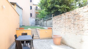 A patio area with a table and chairs, a brick wall, and a small garden. - Borgo San Pietro Garden (Bologna)