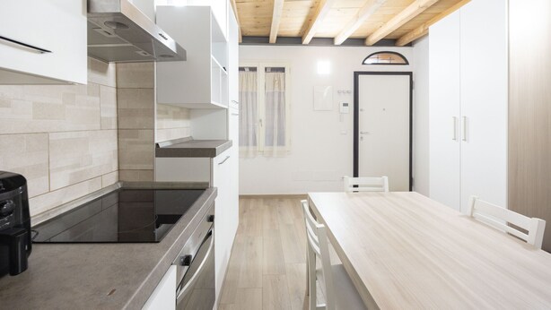A modern kitchen with a wooden ceiling, a dining table, and a white door. - Borgo San Pietro Garden (Bologna)