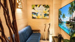 A room with a blue sofa, a painting of flowers, a TV screen with a beach scene, and a small table with a lamp and decorative items. - Hotel BaliBali Sendai (Sendai)