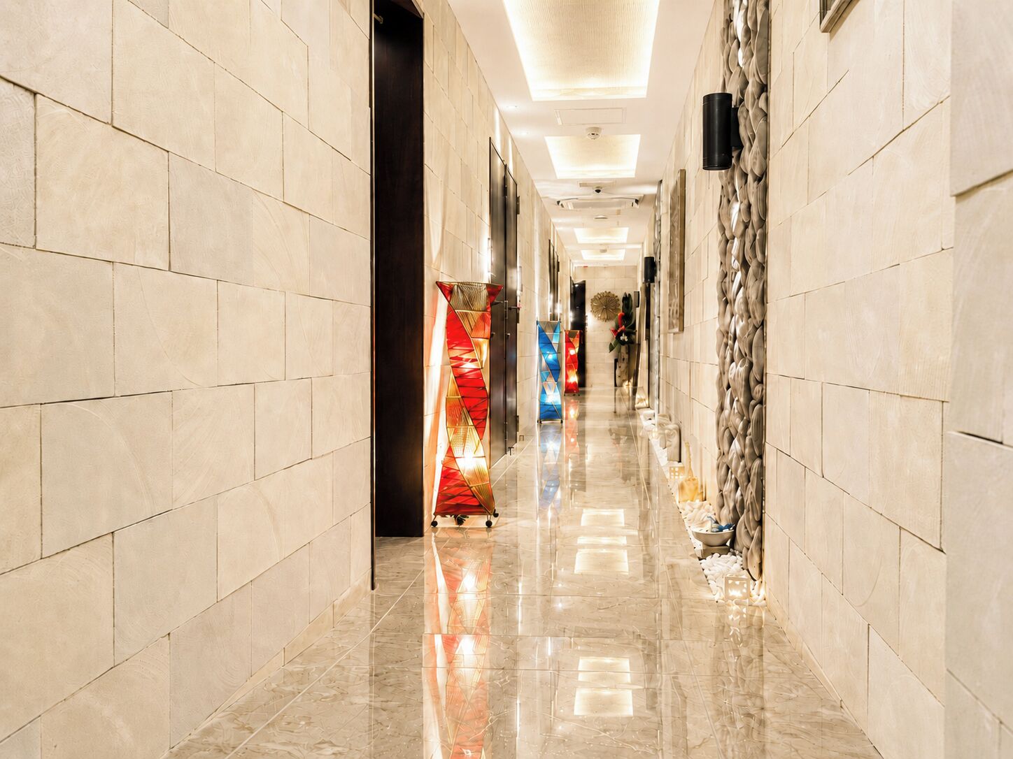Un pasillo de hotel con paredes de baldosas, piso pulido y una lámpara decorativa.