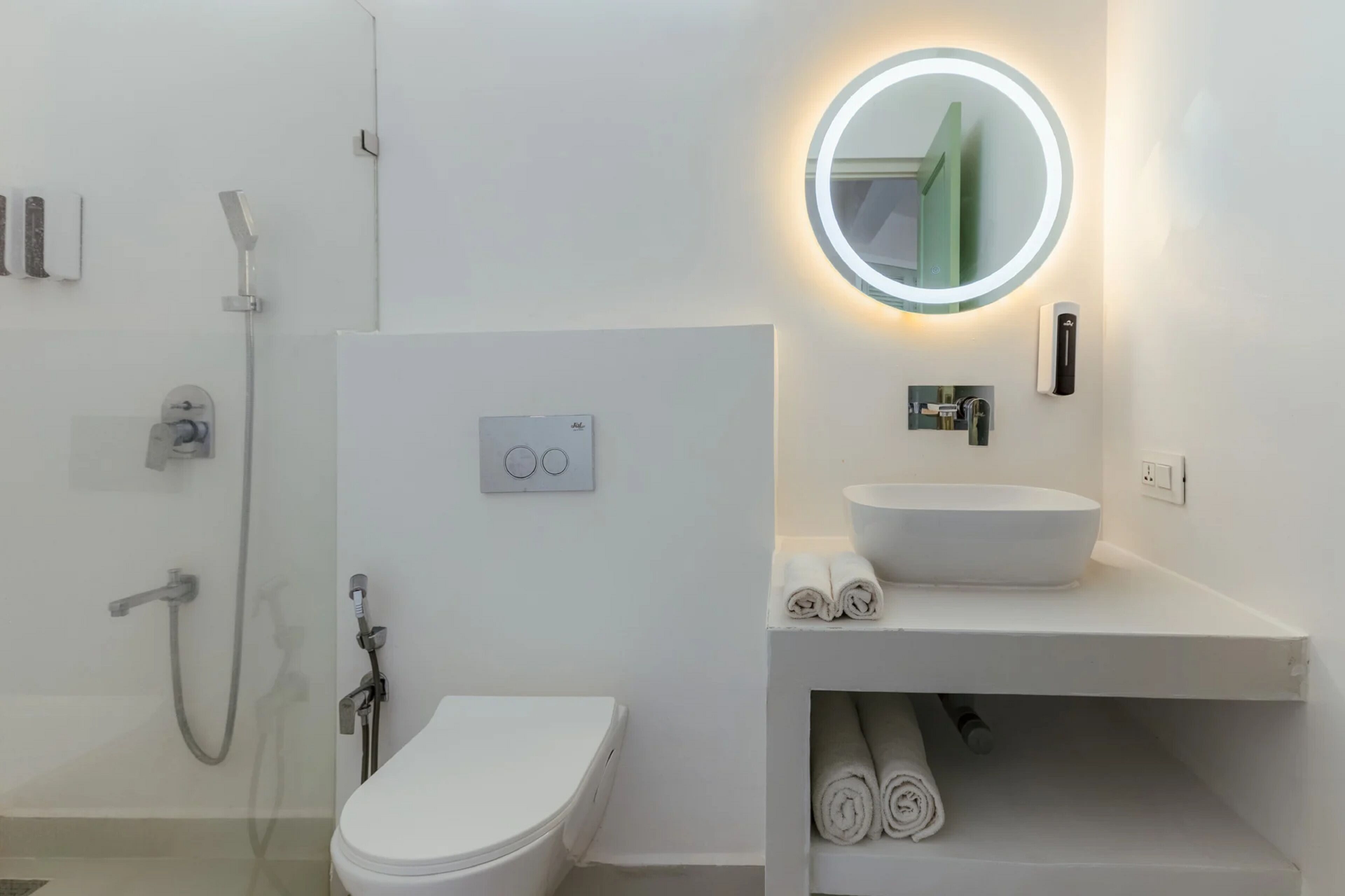 Un baño moderno con inodoro, lavamanos, ducha y espejo con luz circular.