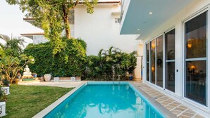 A rectangular swimming pool with a tiled deck, surrounded by lush greenery and a statue. - Aroha Palms Luxury Apartments (Mandrem)