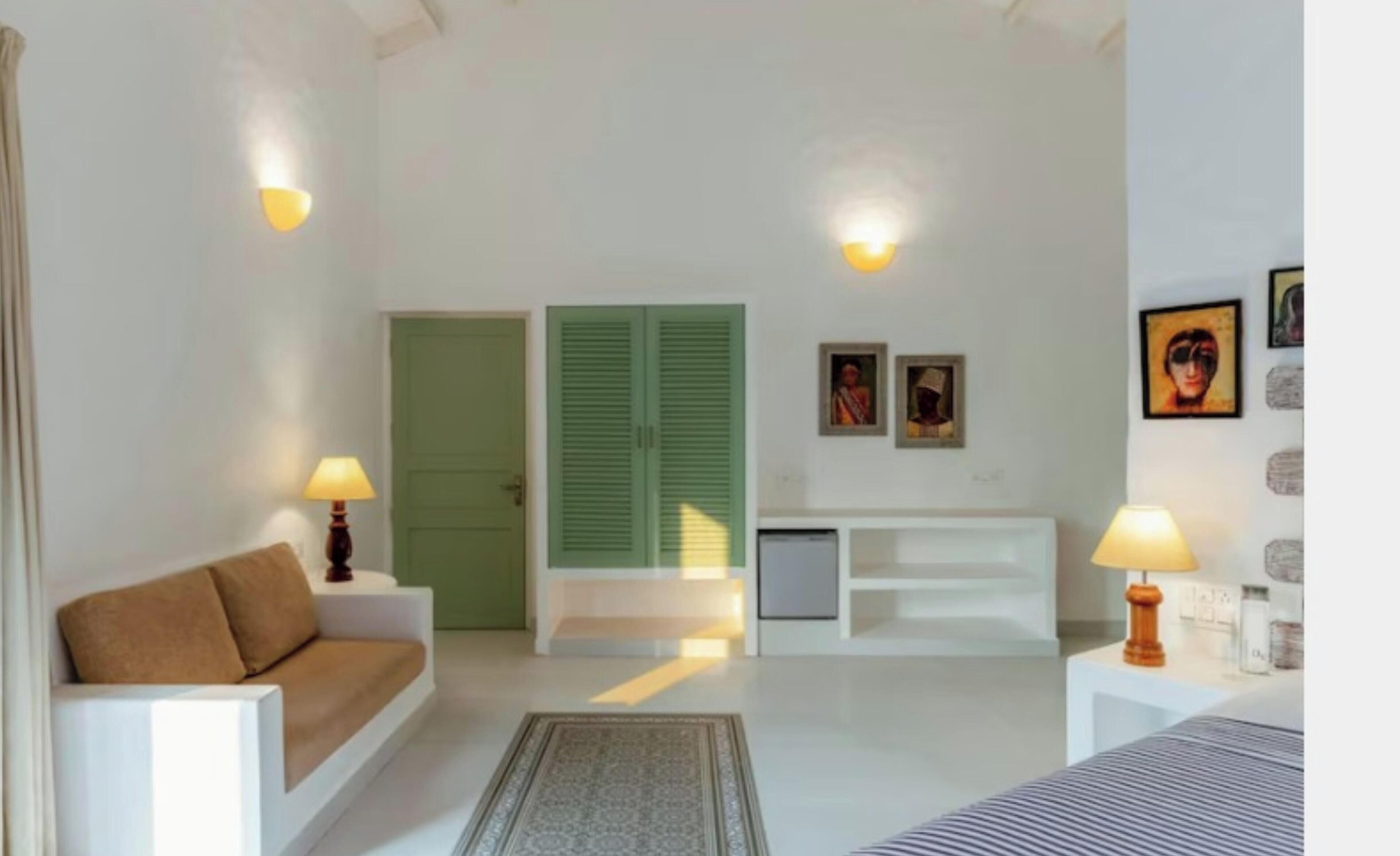 Una habitación con sofá, cama, escritorio, lámpara, puerta y pared decorada con cuadros.