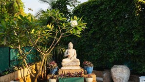 A Buddha statue on a pedestal surrounded by potted plants and a large vase. - Aroha Palms Luxury Apartments (Mandrem)