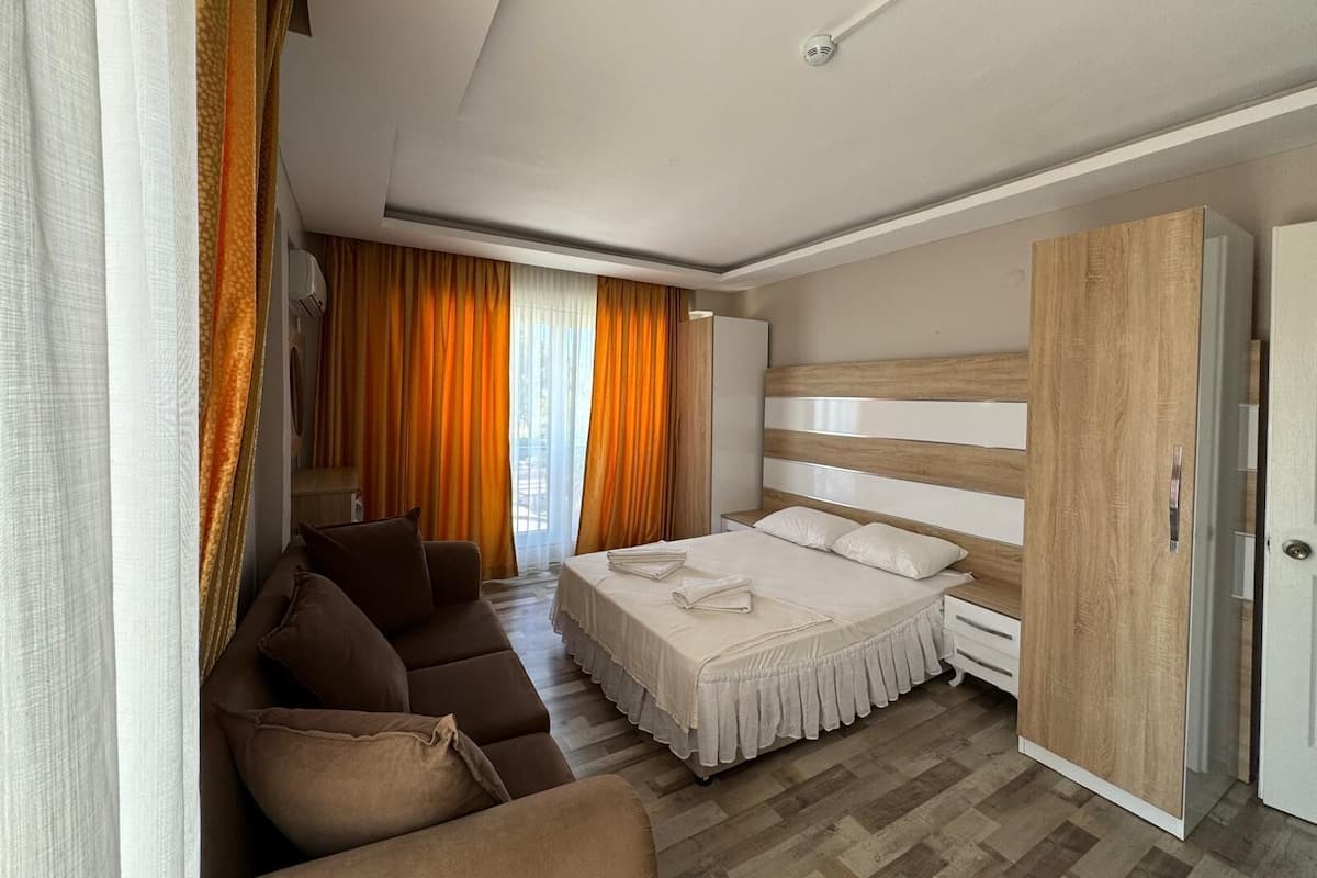 A modern hotel room with a bed, a sofa, a wardrobe, and a view of the outdoors.