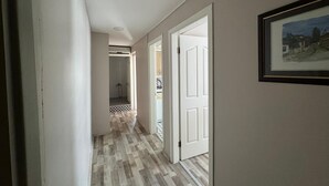Un pasillo con piso de madera, paredes blancas y una puerta que da a un baño con ducha.