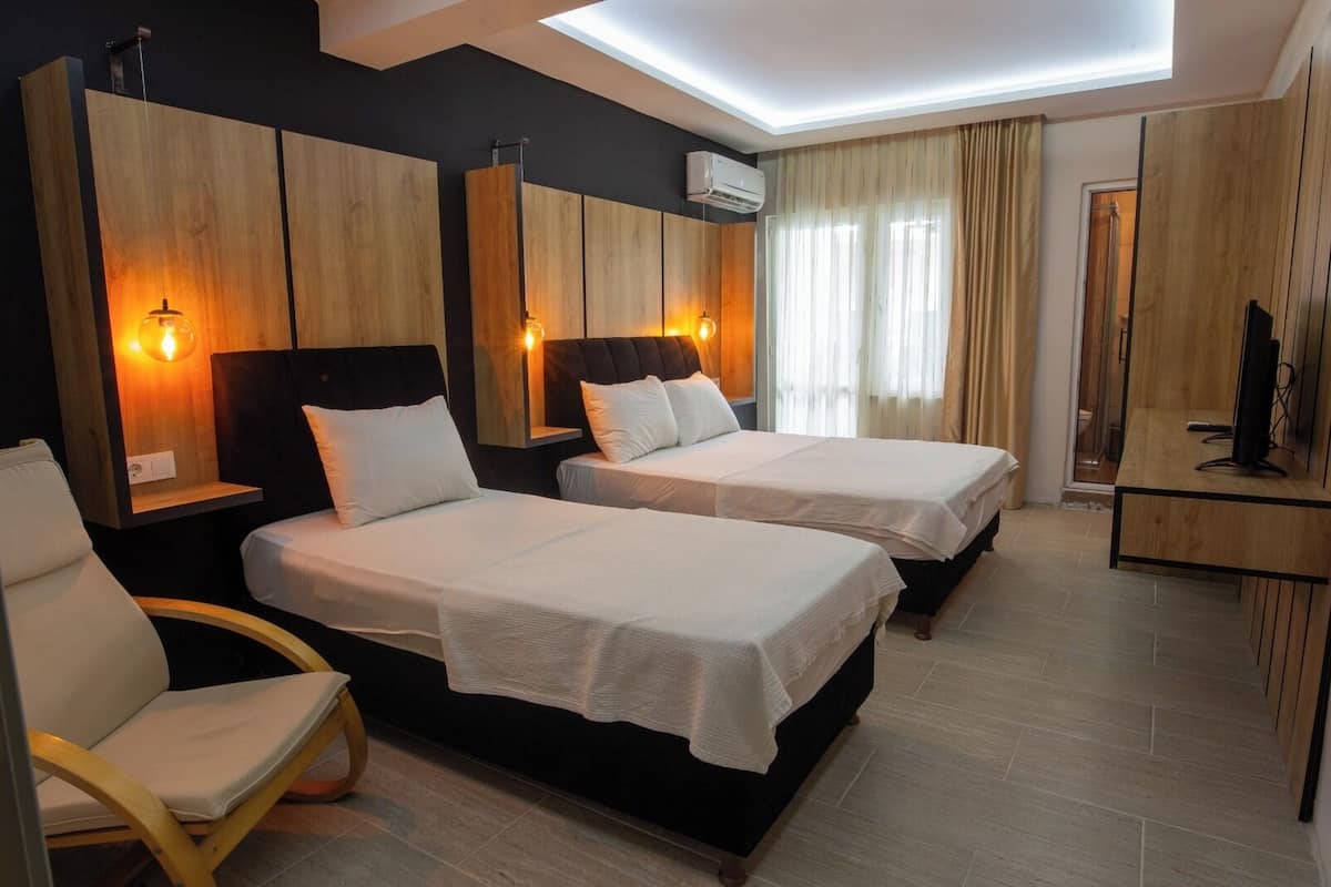 A hotel room with two beds, a chair, a desk, and a TV.