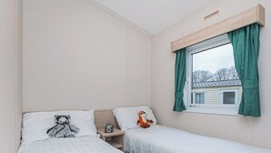 Un dormitorio con dos camas, una ventana con cortinas, una mesita de noche y un peluche.