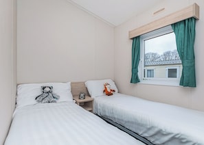 Une chambre avec deux lits, une fenêtre avec des rideaux, une table de chevet et un jouet en peluche.