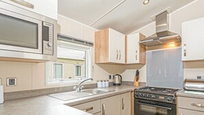 Una cocina compacta con microondas, estufa, horno y una ventana con persianas.