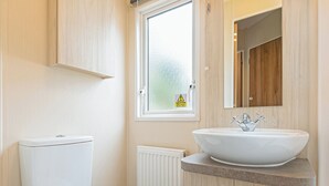 Un baño moderno con inodoro, un lavabo blanco con recipiente y una ventana con vidrio esmerilado, además de un espejo sobre el lavabo.