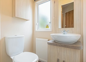 Une salle de bain moderne comprenant des toilettes, un lavabo blanc avec un receveur, une fenêtre à verre dépoli et un miroir au-dessus du lavabo.