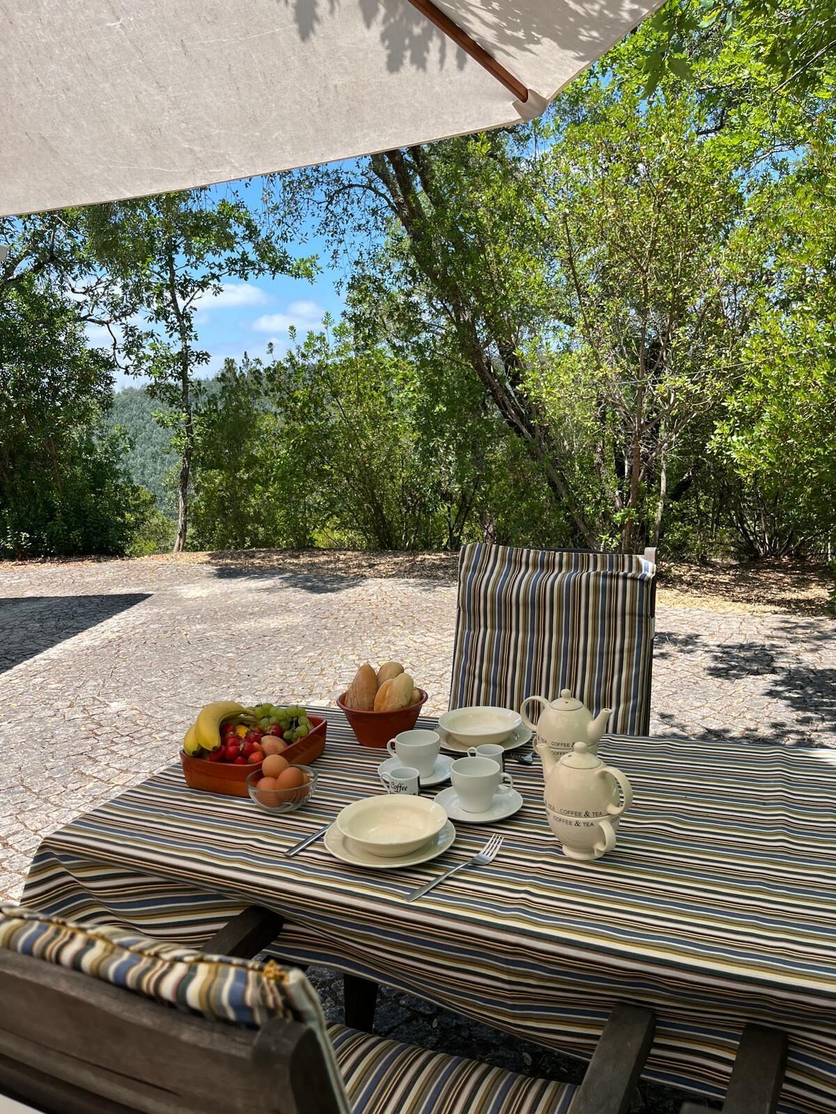 Un área de comedor al aire libre con una mesa preparada para el desayuno, que incluye frutas, pan y café.
