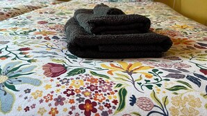 A bed with a floral-patterned bedspread, two pillows with a similar design, and a folded dark-colored towel on the bed.