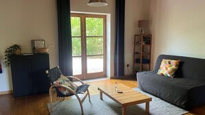 A living room with a sofa, a wooden coffee table, a chair, a bookshelf, and a window with curtains.