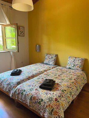 Un lit double avec une literie à motifs floraux, une lampe de chevet et une fenêtre avec des rideaux.