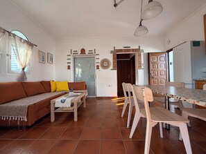 Ein Wohnzimmer mit einer Couch, einem Couchtisch, einem Esstisch, Stühlen und einer Tür zu einem weiteren Raum.