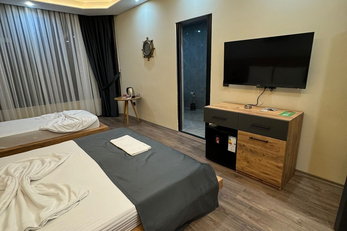 Una camera d'albergo moderna con due letti, una televisione, un tavolino e un armadietto.