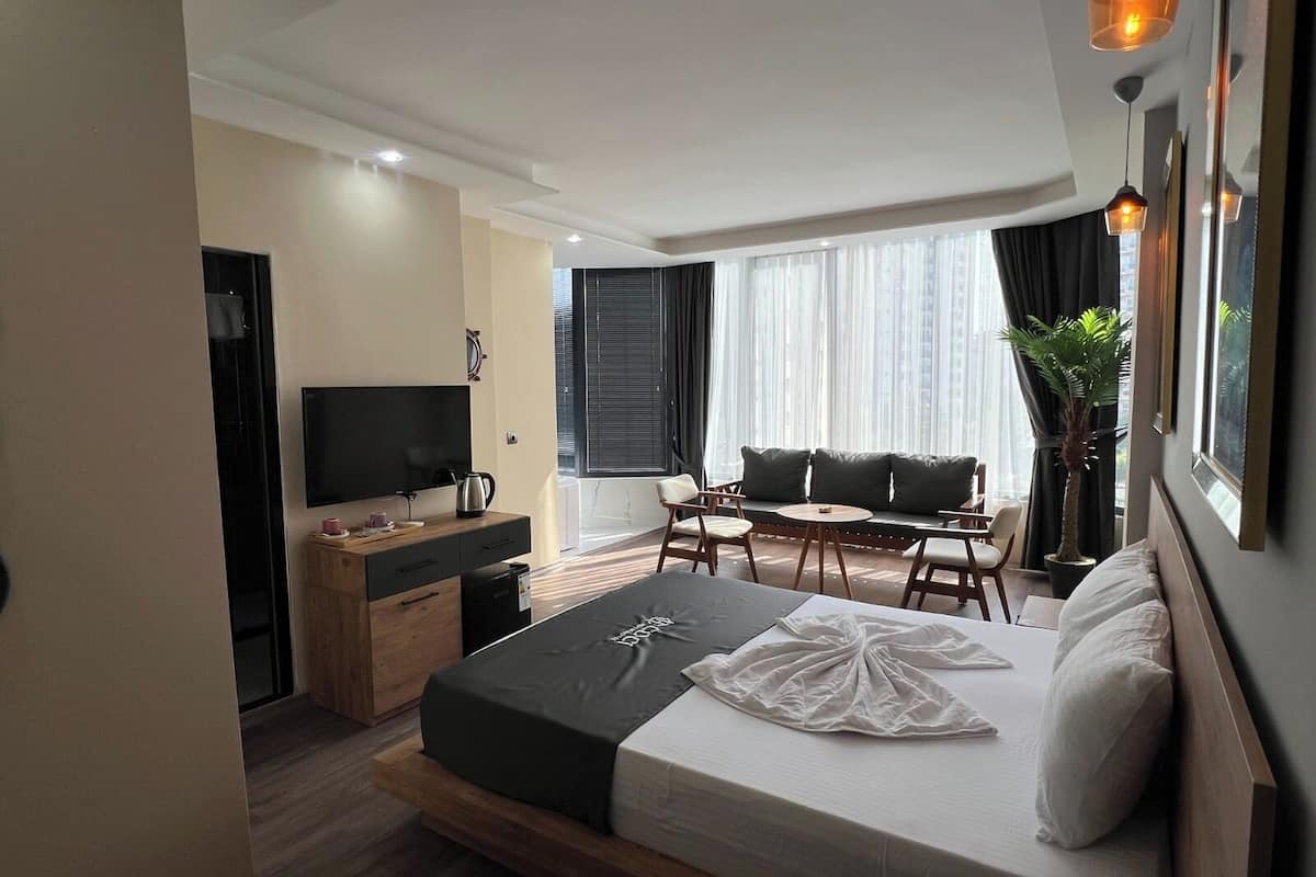 A modern hotel room with a bed, a desk, a television, a sofa, and a window with curtains.