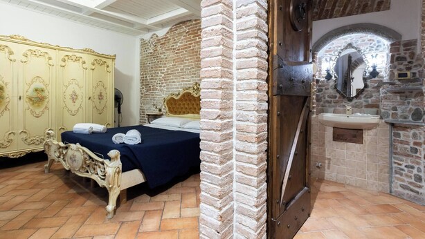 Ein Schlafzimmer mit Bett, Schrank, Steinwand und Badezimmer mit Waschbecken und Spiegel.