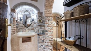 Ein Badezimmer mit Steinwand, Waschbecken, Spiegel und Korbwäsche auf Regalen.