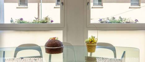 Un espace repas avec une table en verre, des chaises transparentes et une vue sur les bâtiments par une fenêtre.