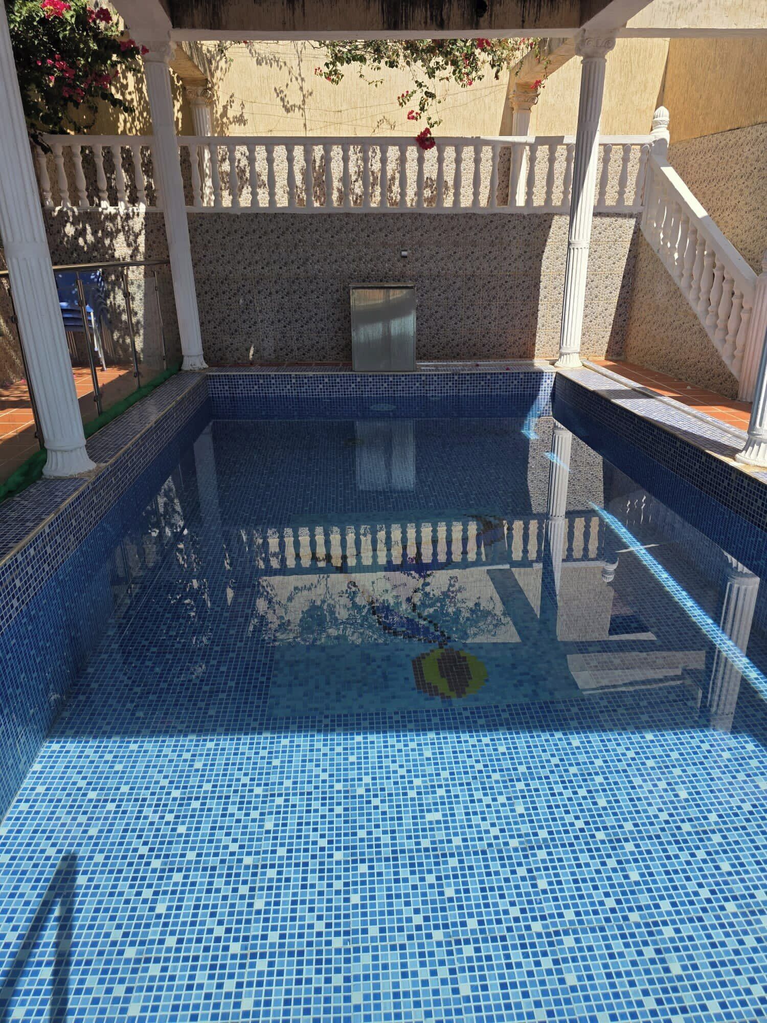 En swimmingpool med blå mosaikfliser, hvide søjler og en stenvæg.