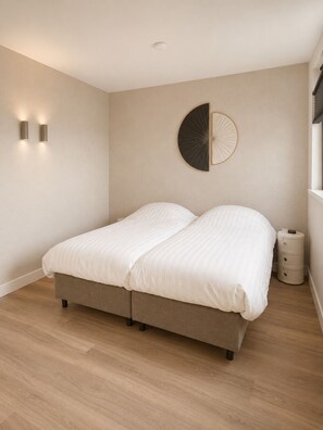 A bedroom with a bed, two wall-mounted lights, a round wall decoration, and a bedside table. - Waterfront villa with a jacuzzi and sauna (Leimuiden)