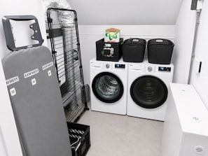 A laundry room with two washing machines, a drying rack, and a storage unit.