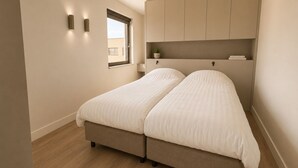 A bedroom with a double bed, a window, a bedside table, and built-in storage cabinets.