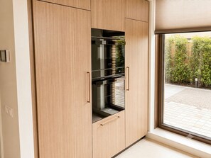 Eine moderne Küche mit Holzausstattung, einem eingebauten Backofen und einem Fenster mit Blick auf einen Garten.