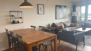 A modern living room with a wooden dining table, black chairs, a grey sofa, and a grey armchair. There is a globe on the table, a framed picture on the wall, and a large abstract painting. - 5 Star Holiday Home in Uddevalla (Uddevalla)
