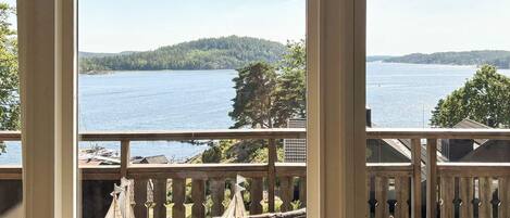 A view from a room with a large window overlooking a lake, with a deck and outdoor furniture visible.