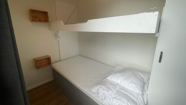A bunk bed room with a wooden headboard, a small wooden shelf, and a white wall. - 5 Star Holiday Home in Uddevalla (Uddevalla)