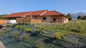 Uma casa de dois andares com telhado de telhas vermelhas, cerca de madeira e um veículo estacionado na frente.