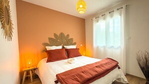 Cama bem arrumada com cabeceira, luminária de cabeceira e janela com cortinas.