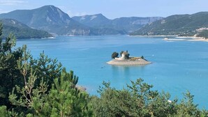 Um lago com uma pequena ilha onde se destaca um edifício, cercado por montanhas e árvores.
