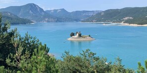 A lake with a small island featuring a building, surrounded by mountains and trees. - The Adri of the Peaks (Chorges)