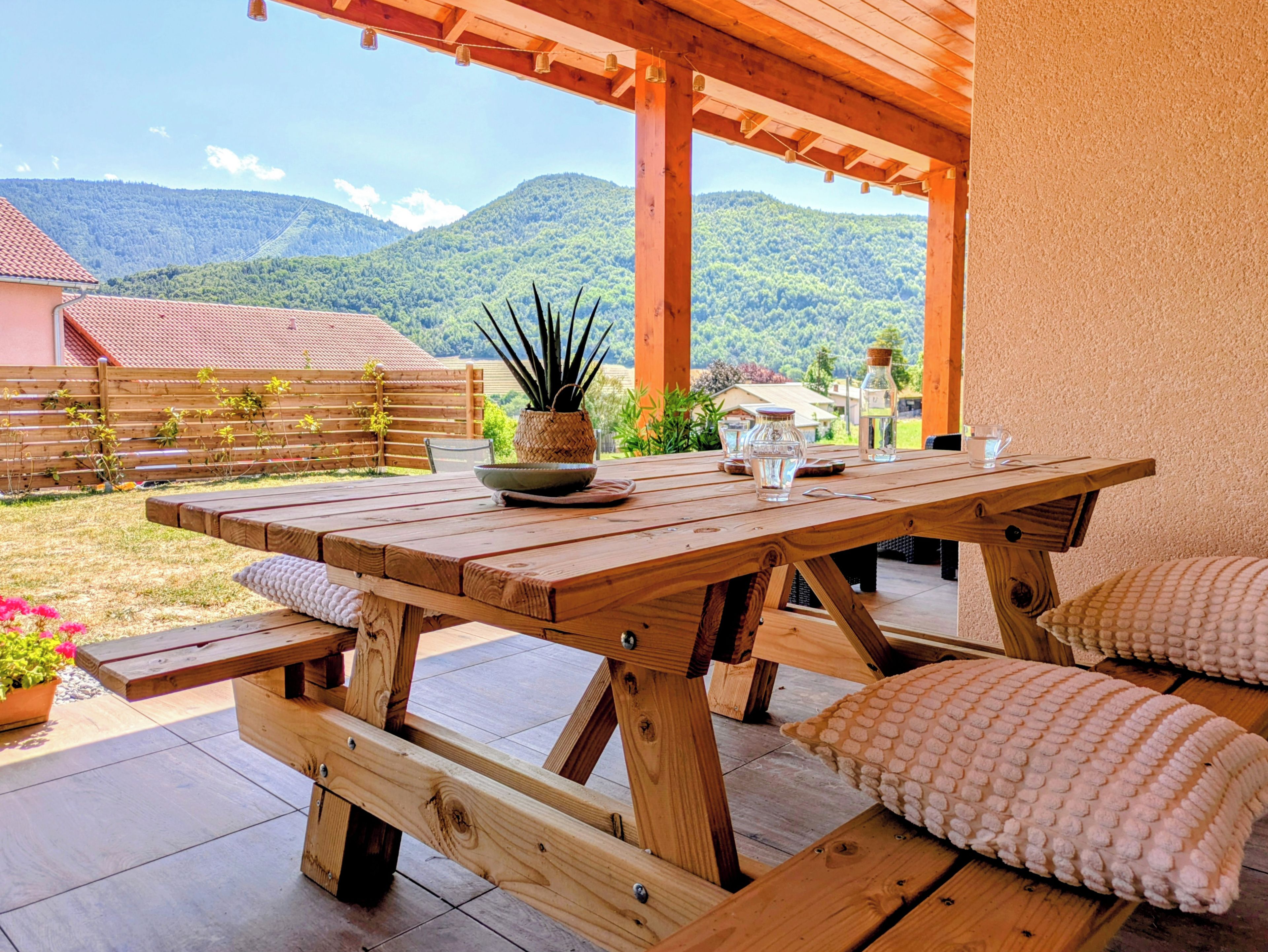 Una mesa de madera al aire libre con bancos, una planta en maceta y vistas a un paisaje montañoso.