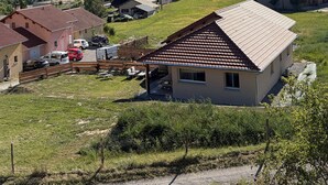 Uma casa de campo com telhado de cerâmica, cercada por um quintal murado, e uma montanha ao fundo.
