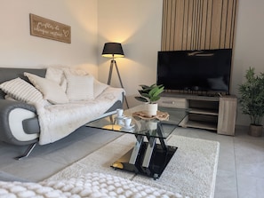 Un salon moderne avec un canapé, une table basse en verre, un téléviseur et une lampe.
