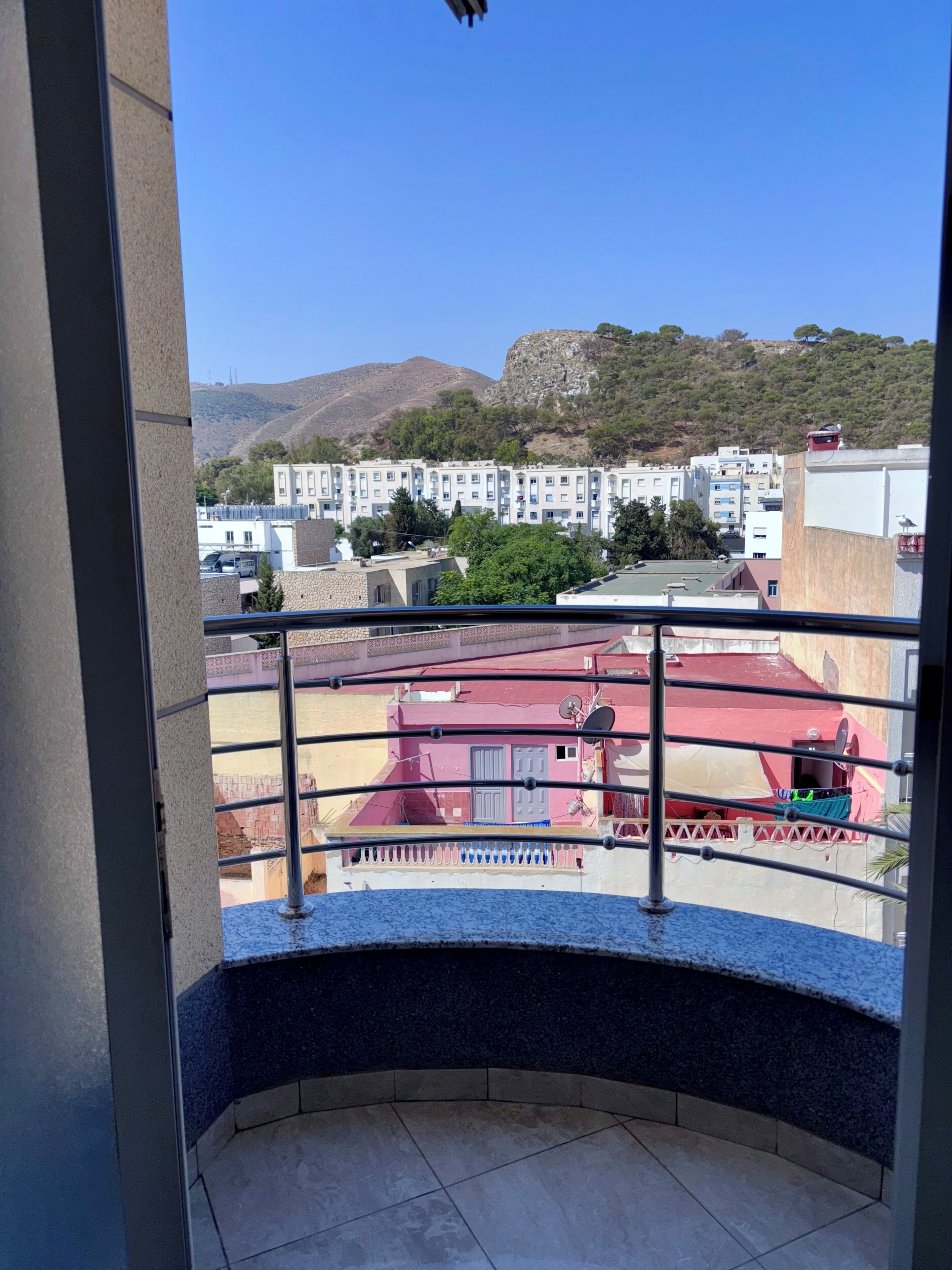 A balcony with a view of a residential area, including buildings and a hill.