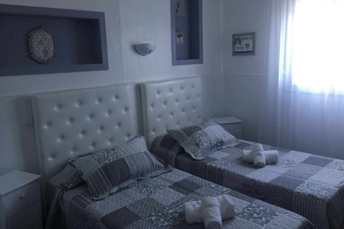 A bedroom with two beds, a headboard, bedside tables, and a window with curtains.