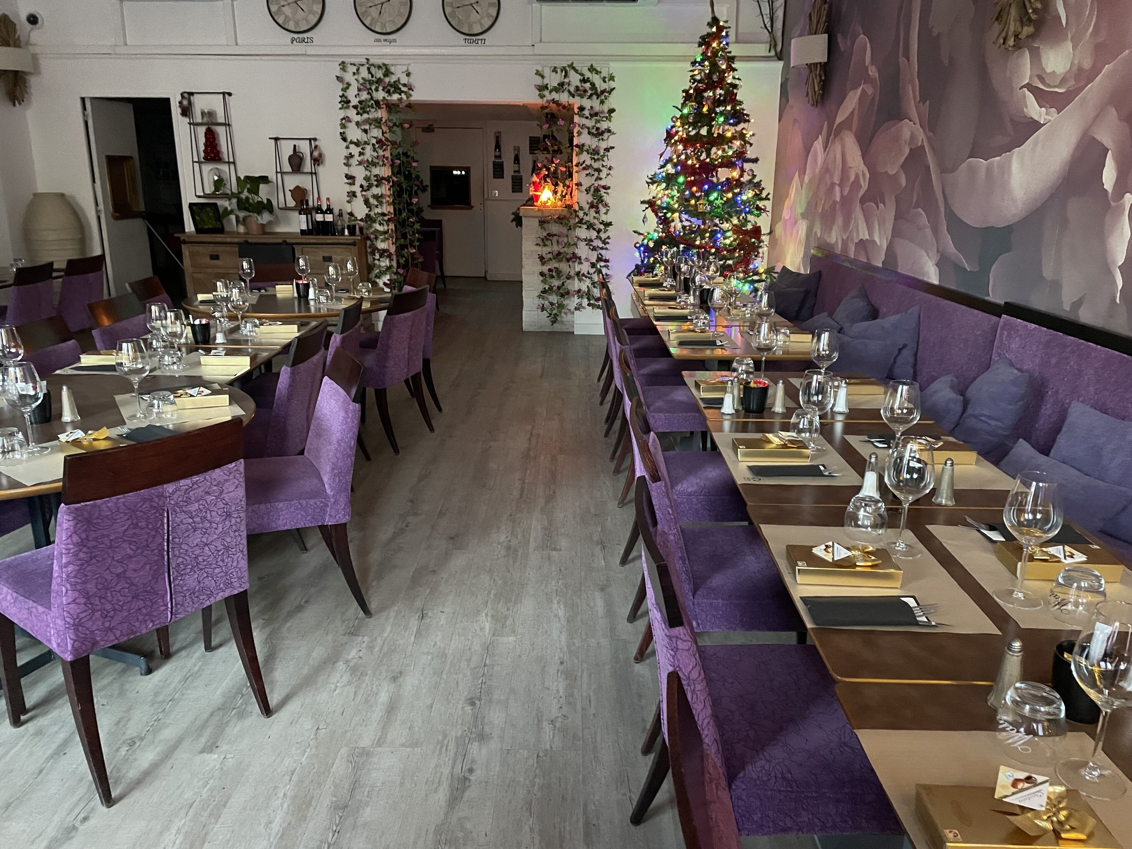 Ein Restaurant mit langen Gemeinschaftstischen, violett gepolsterten Stühlen und einem Weihnachtsbaum.