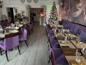 A restaurant with long communal tables, purple upholstered chairs, and a Christmas tree. - luberon hotel restaurant family (Apt)