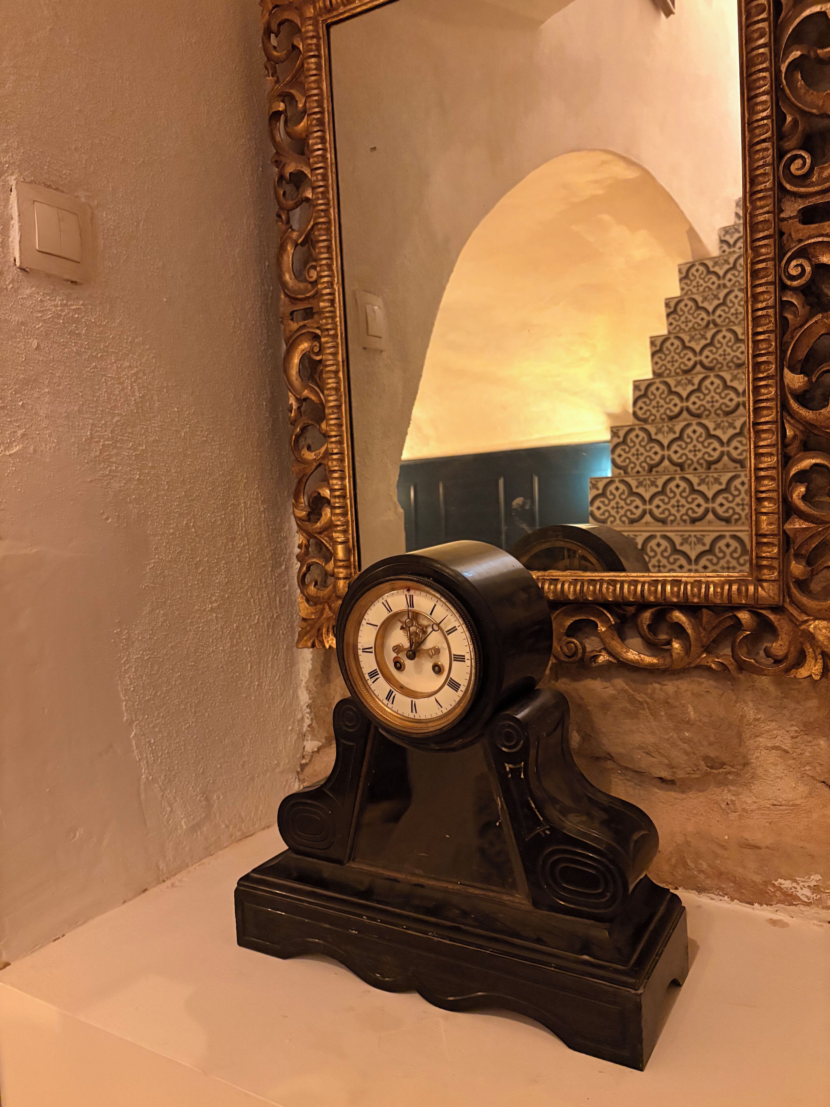 Une horloge murale au design classique, un miroir décoratif doté d’un cadre orné et un mur à motifs en arrière-plan.