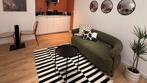 A modern living room with a sofa, a coffee table, a striped rug, a dining area with a kitchen in the background, and a potted plant.