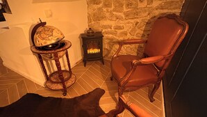A cozy room with a stone wall, a fireplace, a leather armchair, a wooden table with a globe, and a small heater.