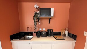A compact kitchen with white cabinets, a microwave, a sink, and a coffee maker.
